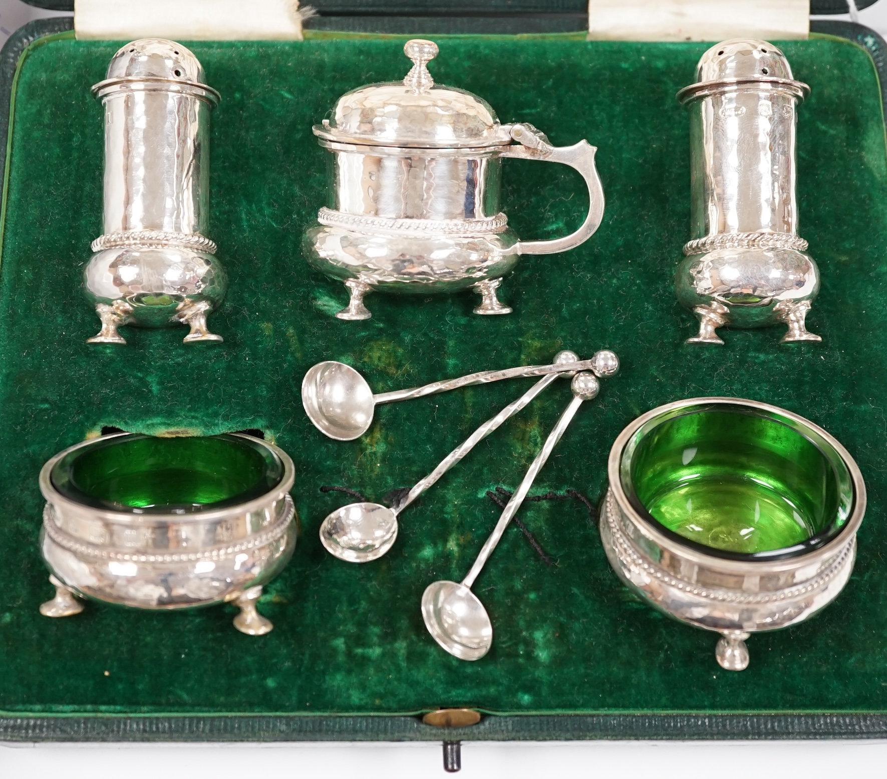 A cased George V planished silver five piece condiment set and three matching spoons by A.E. Jones, Birmingham, 1911.
